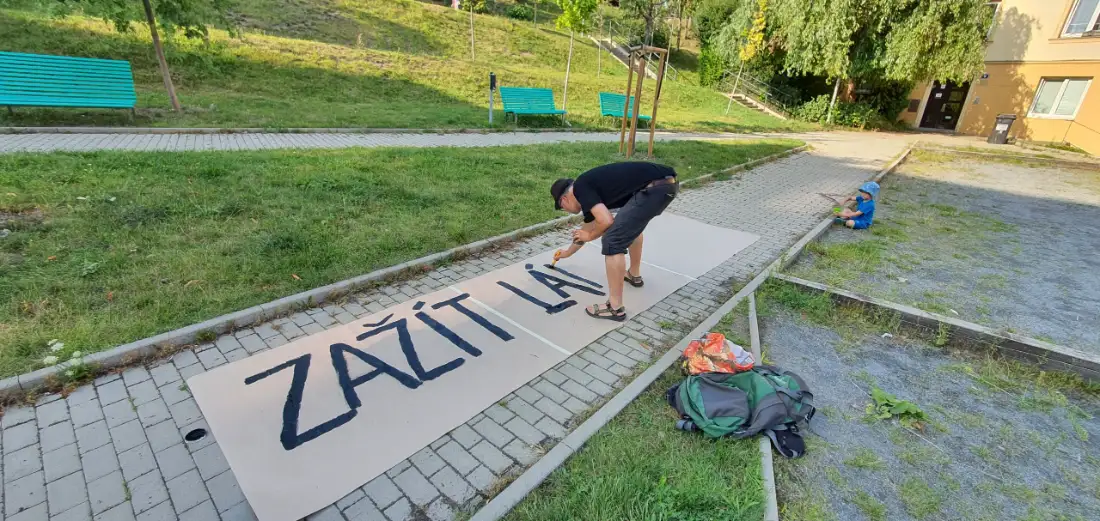 Soused maluje na balicí papír transparent s nápisem Zažít Lán